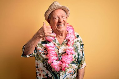 Beyaz saçlı, yaz şapkası takan ve sarı arka planda Hawaii zambağı takan gülümseyen, el ve parmaklarıyla telefonla konuşan yaşlı bir adam. İletişim kavramları.