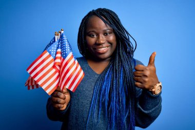 Genç vatansever Afro-Amerikan artı Birleşik Devletler bayrakları taşıyan örgülü kadın gülümsüyor. Tamam işareti yap, başparmağını kaldır, mükemmel işaret.