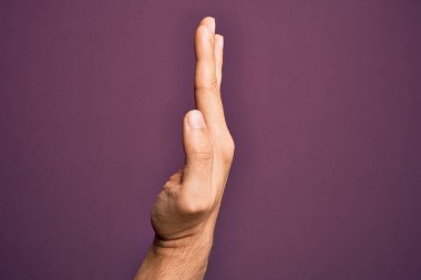 İzole edilmiş mor arka planda parmaklarını gösteren beyaz bir gencin eli uzatılmış el hareketlerini gösteriyor.