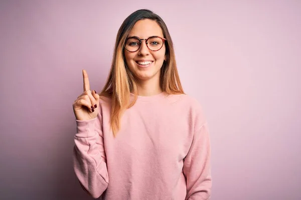 Piękna Blondynka Niebieskimi Oczami Nosząca Sweter Okulary Różowym Tle Pokazując — Zdjęcie stockowe