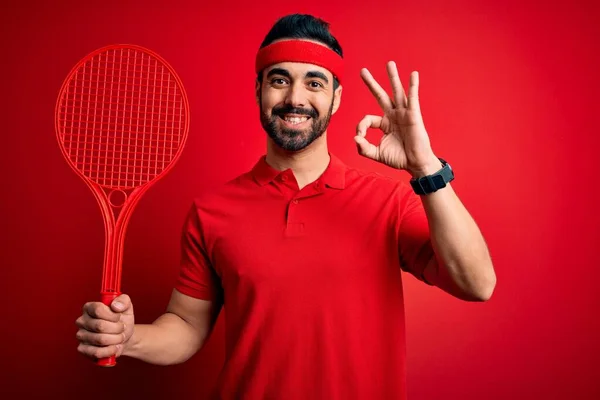 若いですハンサムなスポーツマンとともにひげ再生テニス使用ラケット上の赤の背景を行います指でOkサイン 優れたシンボル — ストック写真