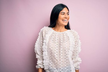 Pembe arka planda zarif bir tişört giyen, yüzünde gülümseme ve doğal bir ifadeyle yan yana duran genç, güzel İspanyol moda kadını. Kendinden emin gülen.