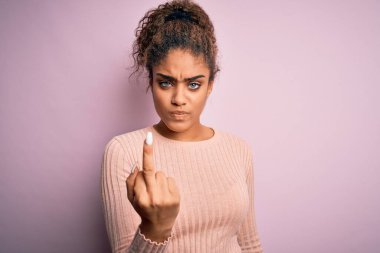 Young beautiful african american girl wearing casual sweater standing over pink background Showing middle finger, impolite and rude fuck off expression