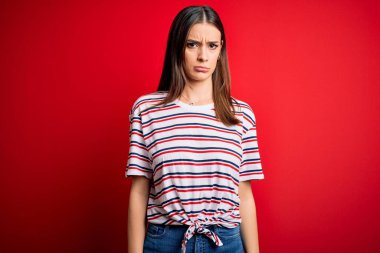 Genç, güzel, esmer, sıradan çizgili tişört giyen, kırmızı arka planda duran, kuşkucu ve gergin, sorun yüzünden üzgün bir kadın. Negatif kişi.