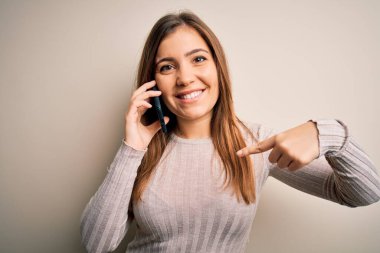 Akıllı telefondan konuşan genç bir kadın izole bir arka planda sürpriz bir yüz ifadesiyle kendini işaret ediyor.