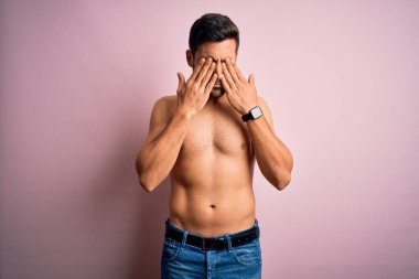 Sakalsız, genç ve güçlü bir adam pembe arka planda duruyor yorgunluk ve baş ağrısı için gözlerini ovuşturuyor, uykulu ve yorgun bir ifade takınıyor. Görüş sorunu