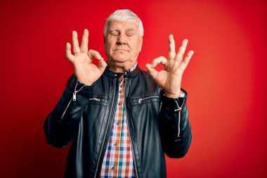 Ayrı kırmızı arka plan üzerinde günlük gömlek ve ceket giyen kıdemli yakışıklı beyaz adam rahatla ve gözün kapalı gülümse parmaklarınla meditasyon hareketi yap. Yoga konsepti.