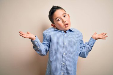 Soyutlanmış arka planda duran zarif tişörtlü, kafası karışmış, kolları ve elleri havada genç bir çocuk. Şüphe kavramı.