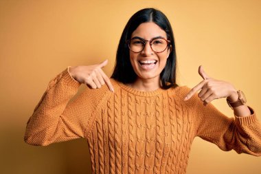 Sarı arka planda gözlük takan genç ve güzel bir İspanyol kadın. Yüzünde bir gülümsemeyle kendinden emin görünüyor. Kendini gururlu ve mutlu bir şekilde gösteriyor..