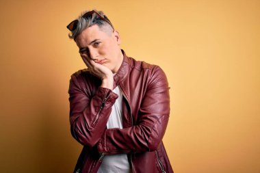 Sarı arka planda moda deri ceketi ve güneş gözlüğü takan genç ve modern bir adam kollarını kavuşturarak depresyondan sıkılmış ve yorgun görünüyor..