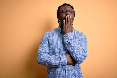 Sarı arka planda gömlek ve gözlük takan genç, Afro-Amerikan adam esnemekten sıkılmış, ağzını eliyle kapatmaktan sıkılmış. Huzursuz ve uykulu..