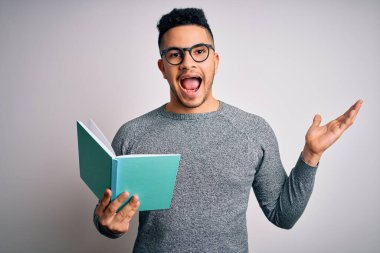 Genç, yakışıklı, zeki bir öğrenci, izole edilmiş beyaz arka planda kitap okuyor. Çok mutlu ve heyecanlı, kazanan yüz ifadesi zaferi büyük bir gülümsemeyle kutluyor ve ellerini kaldırıyor.