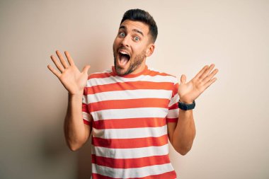 Sıradan çizgili tişört giyen genç yakışıklı adam izole edilmiş beyaz arka plan üzerinde durmuş çılgın ve başarıyı kutlarken kolları havada ve gözleri açık heyecanlı bir şekilde çığlık atıyordu. Kazanan konsept