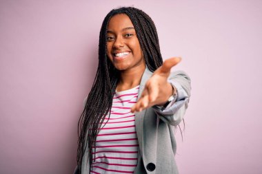 Genç Afro-Amerikan iş kadını pembe izole edilmiş arka planda durup neşeli gülümseyerek yardım eli uzatıyor ve kabul ediyor..