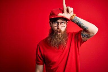 Gözlüklü ve kırmızı şapkalı genç teslimatçı. Alnında parmakları olan insanlarla alay ediyor. Ezik hareketler yapıyor, alay ediyor..