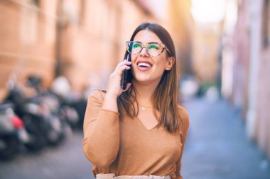 Mutlu ve kendinden emin gülümseyen genç ve güzel bir kadın. Yüzünde gülümsemeyle şehrin akıllı telefonuyla konuşuyor.