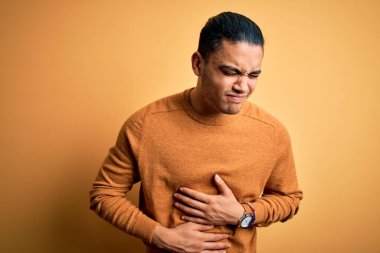 Yalıtılmış sarı arka planda duran sıradan bir süveter giyen genç bir adam midesi üstünde duruyor çünkü hazımsızlık, acı verici bir hastalık, kendini iyi hissetmiyor. Ache kavramı.