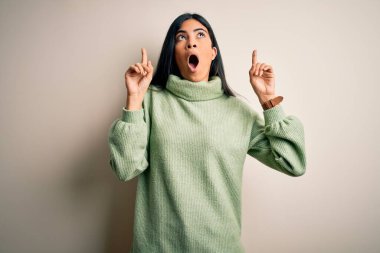 Yeşil kış süveteri giyen genç ve güzel İspanyol bir kadın. Arka planda şaşkın şaşkın ve şaşırmış. Parmaklarıyla işaret ediyor ve kollarını kaldırıyordu..
