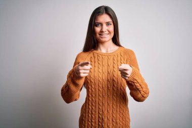 Mavi gözlü genç bir kadın beyaz arka planda dikilip mutlu ve komik yüzlü parmaklarını kameraya doğrultuyor. İyi enerji ve titreşimler.