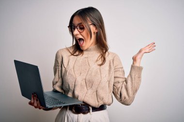 Genç, güzel esmer kadın laptopunu izole edilmiş beyaz arka planda kullanıyor. Çok mutlu ve heyecanlı. Kazanan ifade zaferi büyük bir gülümsemeyle kutluyor.