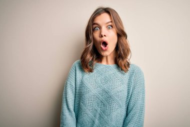 Genç sarışın kız, sakin, mavi bir süveter giyiyor. Arka planda, korku ve şaşkınlık dolu bir ifade var..
