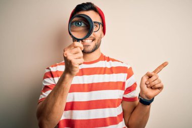 Genç dedektif, izole edilmiş arka planda büyüteçten bakıyor. Çok mutlu bir şekilde el ve parmak kenarı işaret ediyor.