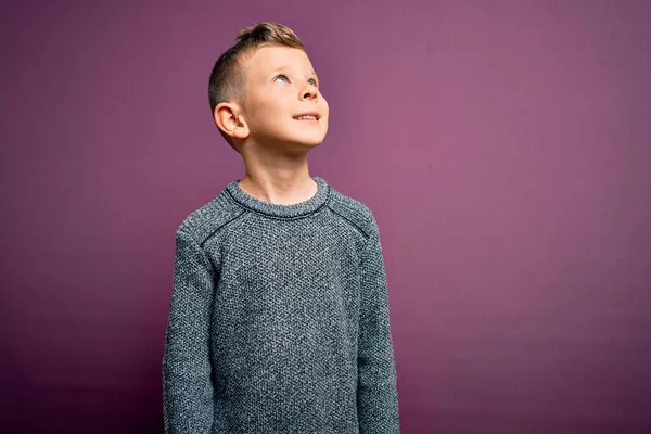 青い目の青い目をした若い白人の子供は 紫色の背景の上に立って冬のセーターを着て顔を笑顔で横に見て 自然な表情 自信を持って — ストック写真