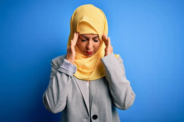 ストレスのために頭痛の種に手で青の背景にイスラム教徒の伝統的なヒジャーブを身に着けている中世のブルネットのビジネス女性 片頭痛に苦しむ — ストック写真