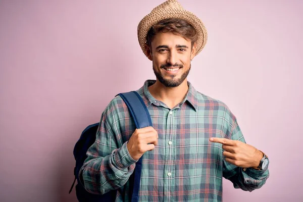 若いです観光客の男オン休暇身に着けているバックパックと夏の帽子以上ピンクの背景とともに驚き顔指摘指へ彼自身 — ストック写真
