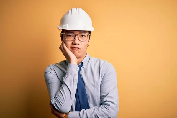 年轻英俊的中国建筑师 戴着安全帽 打着黄色背景的领带 满脑子疲惫不堪 双手交叉 对抑郁症感到厌烦 — 图库照片