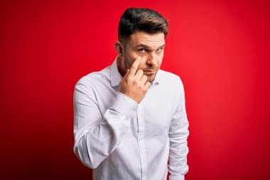 Mavi gözlü, zarif gömlekli genç bir iş adamı. Kırmızı izole edilmiş arka planda dikiliyor. Gözlerine işaret ediyor.