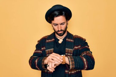 Genç, yakışıklı, bohem, hippi tarzı ve bohem şapkalı bir adam. Kol saatini kontrol ediyor, rahat ve kendinden emin.