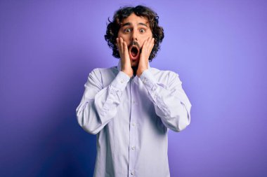 Mor arka plan üzerinde duran sakallı, genç ve yakışıklı iş adamı korkmuş ve şok olmuş, şaşırmış ve şaşkın bir yüz ifadesi var.