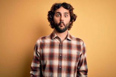 Sakallı, sıradan tişörtlü, sarı arka planda duran genç yakışıklı adam dudaklı balık suratlı, çılgın ve komik bir jest yapıyor. Komik ifade.