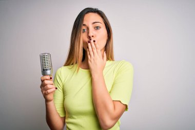 Sarışın, genç bir kadın, izole edilmiş beyaz arka planda ampulü tutuyor. Ağzı kapalı, utancından ağzı açık, korku ifadesi, sessizlikten korkmak, gizli bir konsept.