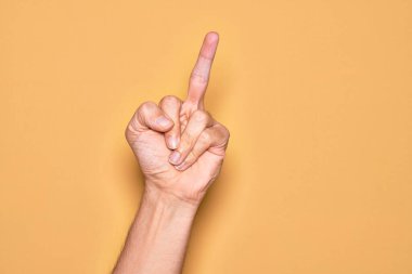 Hand of caucasian young man showing fingers over isolated yellow background showing provocative and rude gesture doing fuck you symbol with middle finger
