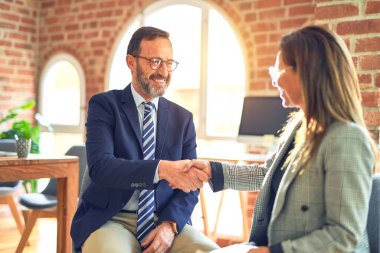 Mutlu ve kendinden emin gülümseyen iki orta yaşlı iş adamı. Birlikte çalışırken gülümseyerek ofiste el sıkışırken.