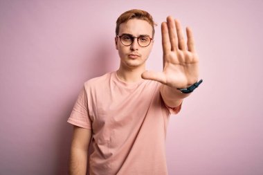 Gayri resmi tişört giyen genç, yakışıklı kızıl adam izole edilmiş pembe arka planda durup avuç içiyle şarkı söylemeyi kesiyor. Yüzünde olumsuz ve ciddi bir jest olan uyarı ifadesi.