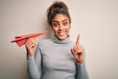 Genç Afro-Amerikan Afro-Amerikan kızı izole edilmiş beyaz arka plan üzerinde kağıt uçak tutuyor. Bir fikir ya da soru işareti ile şaşırdı.
