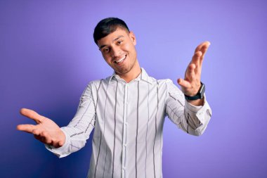 Zarif iş gömleği giyen genç yakışıklı İspanyol adam mor arka planda dikiliyor. Gülümsüyor, yardım eli uzatıyor ve kabul ediyor..