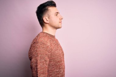 Pembe izole edilmiş arka plan üzerine sıradan bir kazak giyen yakışıklı beyaz bir adam. Yan yana bakıyor, rahat bir görünüm sergiliyor ve kendine güvenen bir gülümseme sergiliyor..