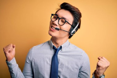 Genç, yakışıklı Çinli çağrı merkezi ajanı, kulaklık takıyor. Çok mutlu ve heyecanlı. Kolları havada, gülümsüyor ve başarı için bağırıyor. Kutlama konsepti.