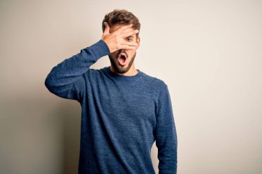 Sakallı, sıradan bir süveter giyen genç bir adam beyaz arka planda dikiliyor. Şok olmuş bir şekilde yüzünü ve gözlerini kapıyor. Utanmış bir ifadeyle parmaklarının arasından bakıyor..