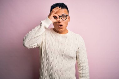 Beyaz süveter giyen, pembe arka planda gözlük takan genç, yakışıklı Latin bir adam şaşırmış yüz ifadesiyle şaşırmış, parmaklarından bakan bir jest yapıyor. İnançsız ifade.
