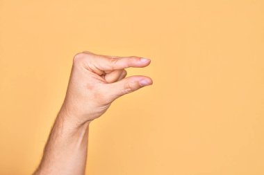 İzole edilmiş sarı arka plan üzerinde parmaklarını gösteren beyaz bir adamın eli. Görünmez bir şeyi alıp, parmaklarıyla uzayı gösteren bir nesneyi tutuyor.