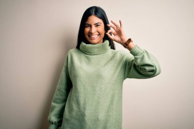 İzole edilmiş arka planda yeşil süveter giyen genç ve güzel İspanyol kadın el ve parmaklarıyla 