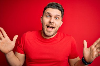 Kırmızı arka plan üzerine günlük tişört giyen mavi gözlü genç adam çılgın ve başarıyı kollarını kaldırıp heyecanla haykırarak kutluyor. Kazanan konsept