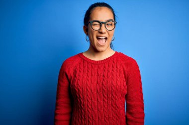 Genç, güzel Asyalı bir kadın mavi arka plan üzerinde gözlük takıyor ve kameraya seksi bir ifadeyle bakıyor, neşeli ve mutlu bir yüzle..