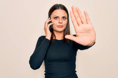 Genç, güzel, esmer bir kadın akıllı telefonla konuşuyor. Eli açık, dur işareti yapıyor. Ciddi ve kendinden emin bir ifadeyle, savunma hareketi yapıyor.