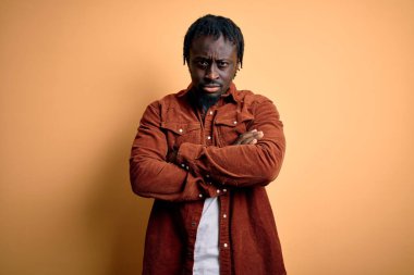 Sarı arka plan kuşkucu ve gergin, kollarını kavuşturup onaylamadığı ifadesini takınan sıradan bir ceket giyen yakışıklı Afro-Amerikan erkeği. Negatif kişi.